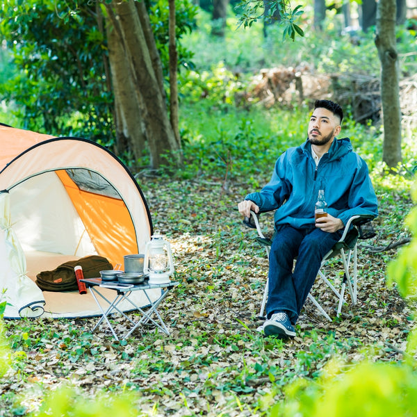 Man sitting in a chair next to a tent in a forest setting